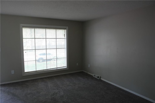 empty room featuring dark carpet, baseboards, and a textured ceiling