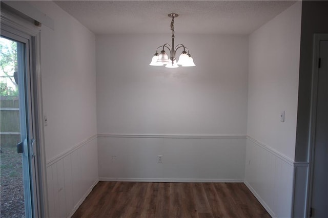 unfurnished dining area with wood finished floors, a chandelier, wainscoting, and a textured ceiling