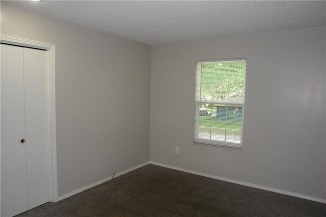 unfurnished bedroom with dark carpet, a textured ceiling, a closet, and baseboards