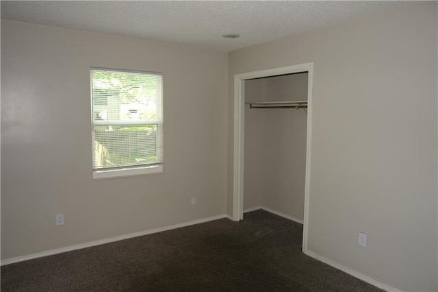 unfurnished bedroom featuring dark colored carpet, a textured ceiling, a closet, and baseboards