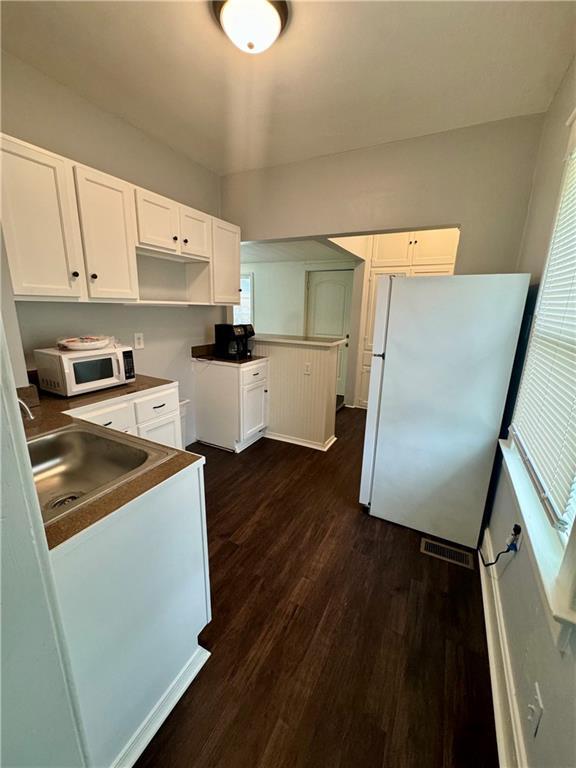 2518 N 12th St, Kansas City, KS 66104 - kitchen with dark wood-type flooring, white cabinets, visible vents, and white appliances