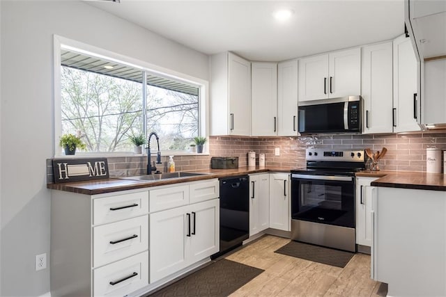 kitchen featuring white cabinets, stainless steel appliances, a sink, light wood-type flooring, and backsplash
