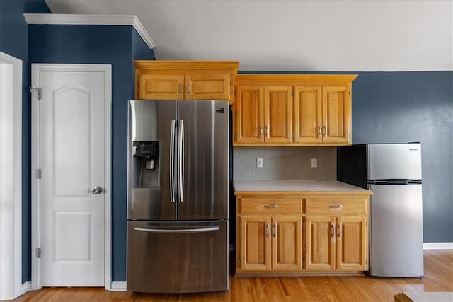 kitchen with stainless steel fridge with ice dispenser, light countertops, light wood-style flooring, freestanding refrigerator, and backsplash