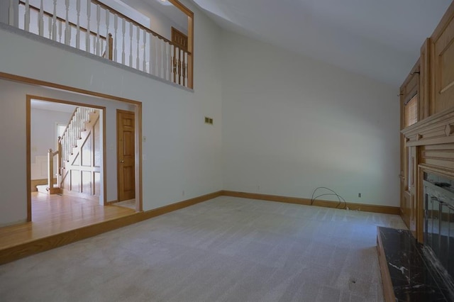 1313 NW 12th St, Blue Springs, MO 64015 - unfurnished living room with light carpet, high vaulted ceiling, a glass covered fireplace, baseboards, and stairway