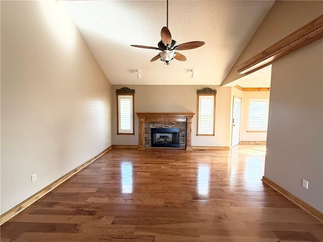 unfurnished living room featuring a fireplace, a textured ceiling, a ceiling fan, wood finished floors, and lofted ceiling