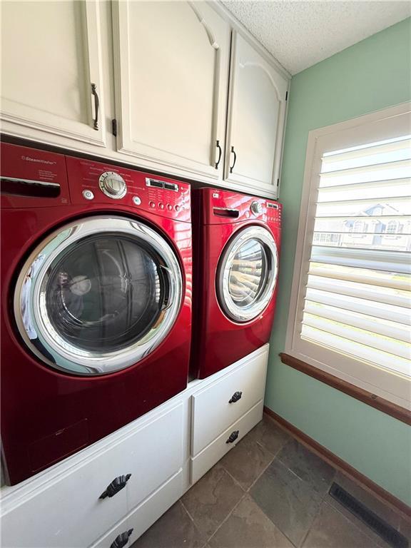clothes washing area with a textured ceiling, separate washer and dryer, visible vents, baseboards, and cabinet space