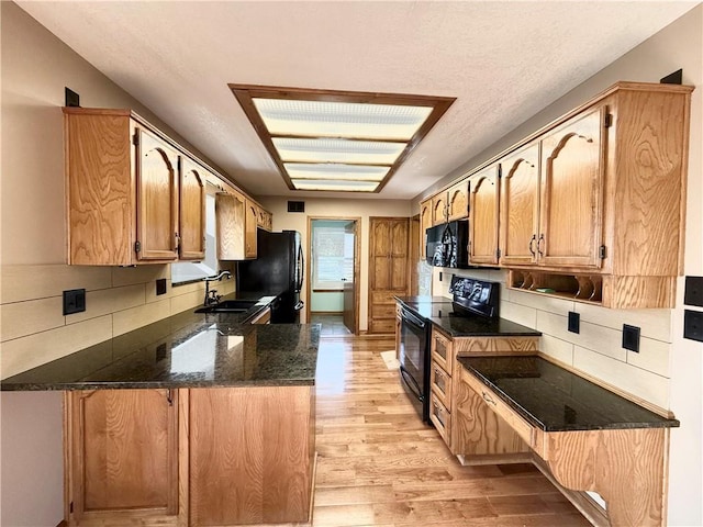 kitchen with light wood-style flooring, a peninsula, tasteful backsplash, black appliances, and a sink