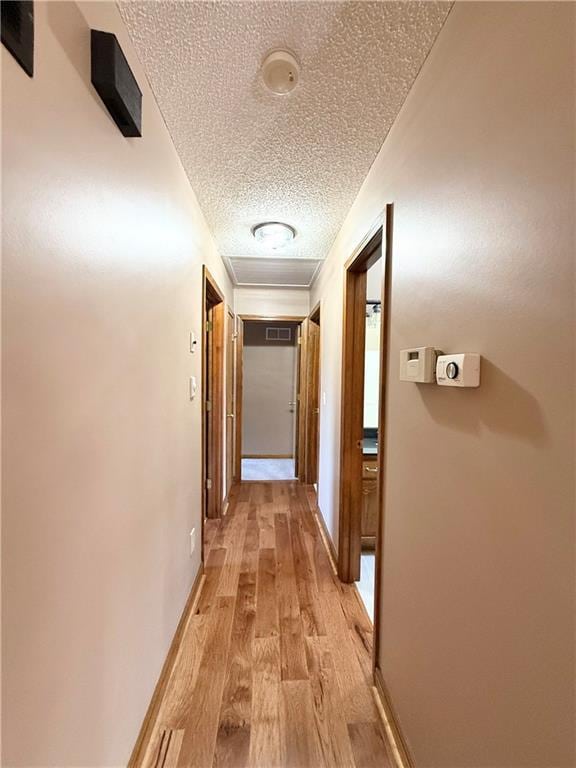corridor featuring a textured ceiling, light wood finished floors, baseboards, and visible vents
