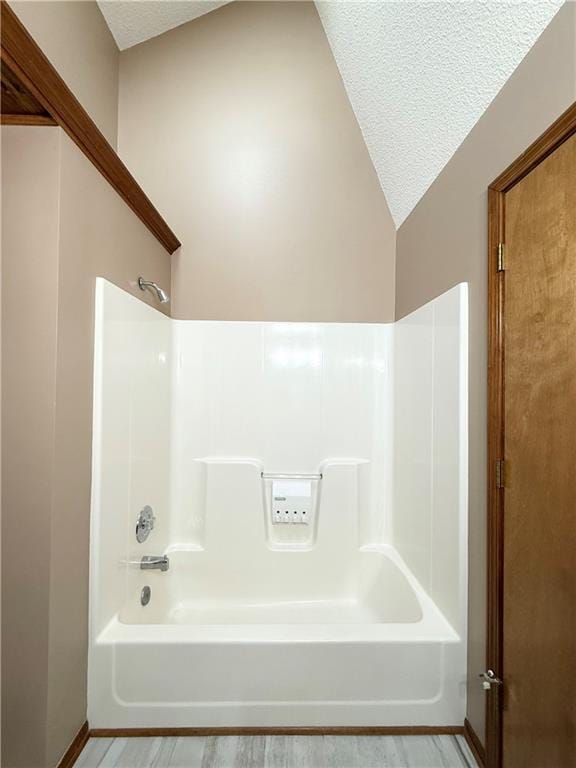 full bath featuring a textured ceiling, wood finished floors, shower / tub combination, and lofted ceiling