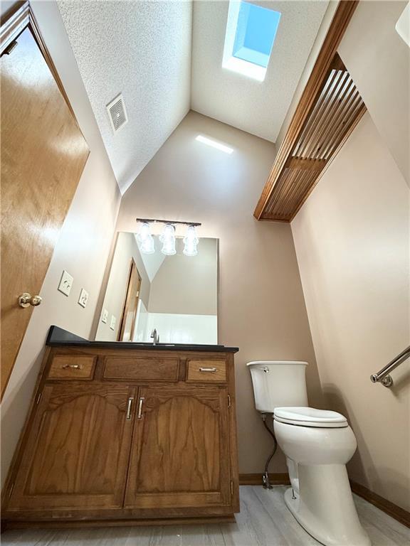 half bath with vanity, vaulted ceiling, a textured ceiling, toilet, and visible vents