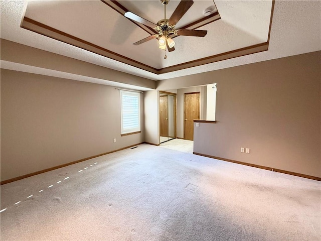 unfurnished bedroom with baseboards, light carpet, a tray ceiling, and a textured ceiling