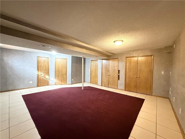 basement with a textured ceiling, tile patterned flooring, and visible vents