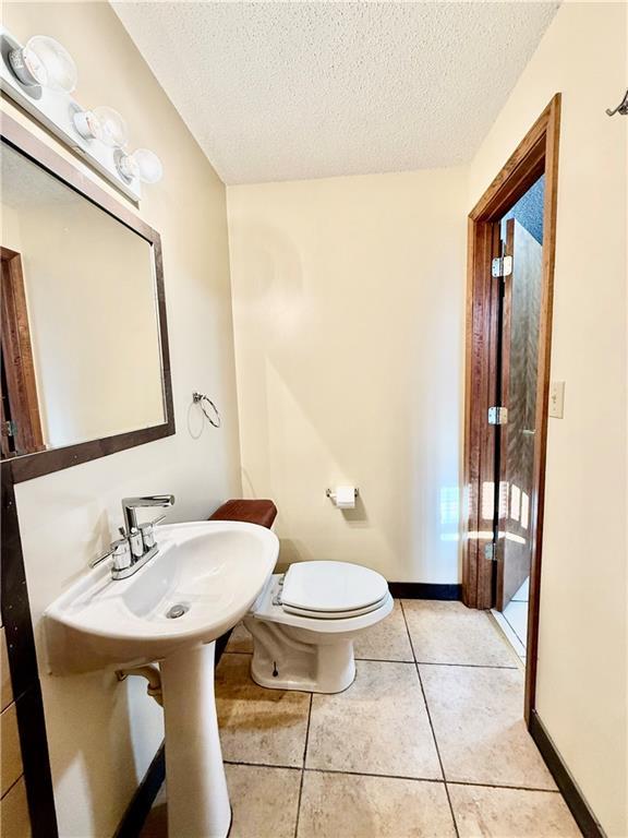 half bathroom featuring toilet, tile patterned flooring, baseboards, and a textured ceiling