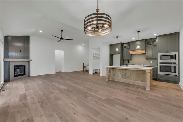 502 Seventh St, Smithville, MO 64089 - kitchen featuring appliances with stainless steel finishes, premium range hood, light countertops, light wood-style flooring, and decorative backsplash