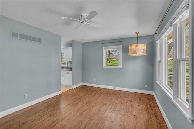 spare room with baseboards, light wood-style flooring, a textured ceiling, a ceiling fan, and visible vents
