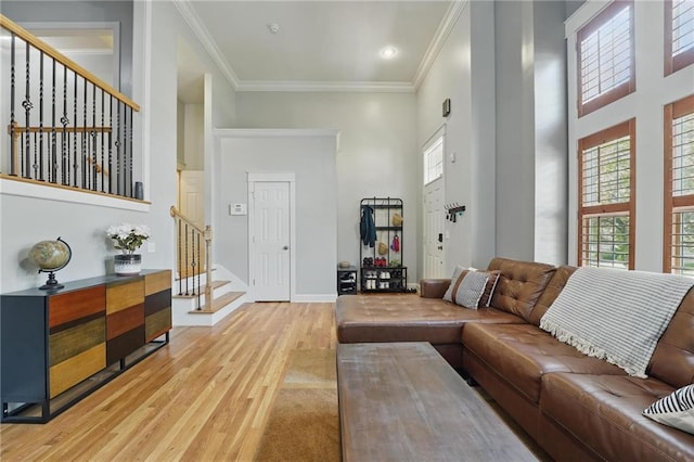living room featuring ornamental molding, stairs, baseboards, a high ceiling, and light wood finished floors