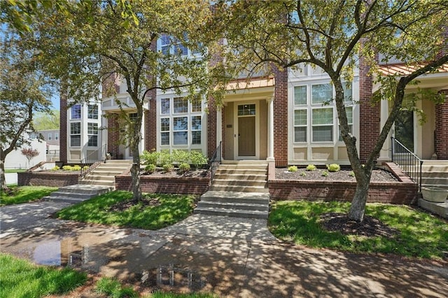 view of property hidden behind natural elements with stairway and brick siding