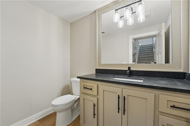 half bathroom with wood finished floors, toilet, vanity, and baseboards