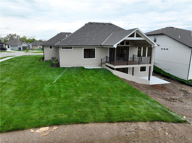 rear view of property featuring a lawn and roof with shingles