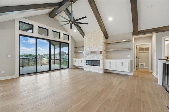 unfurnished living room featuring a ceiling fan, high vaulted ceiling, a stone fireplace, beam ceiling, and light wood-type flooring