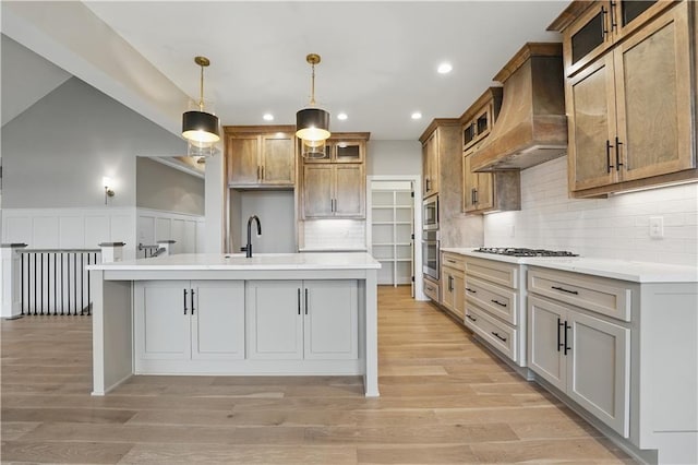 kitchen with custom range hood, gas stovetop, light countertops, an island with sink, and recessed lighting