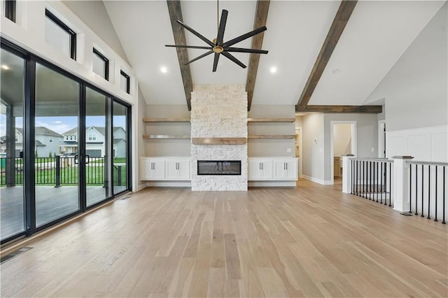 unfurnished living room featuring high vaulted ceiling, ceiling fan, light wood-type flooring, a stone fireplace, and beam ceiling