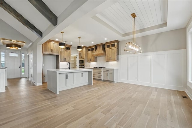kitchen featuring custom exhaust hood, a decorative wall, light countertops, a sink, and appliances with stainless steel finishes