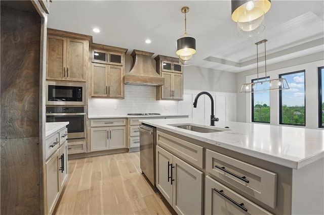 kitchen with appliances with stainless steel finishes, a sink, premium range hood, light wood-type flooring, and decorative backsplash