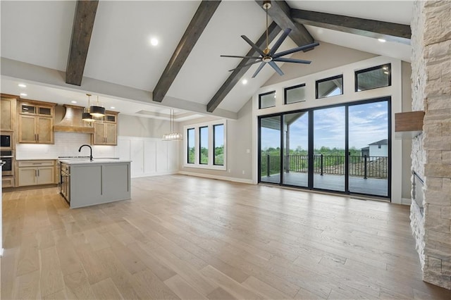 unfurnished living room with a ceiling fan, high vaulted ceiling, beamed ceiling, a sink, and light wood-style floors