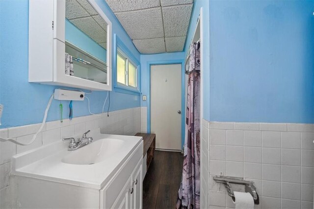 4401 N Holmes St, Kansas City, MO 64116 - bathroom featuring wood finished floors, wainscoting, vanity, a drop ceiling, and tile walls