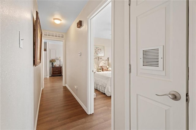 hall featuring visible vents, baseboards, and wood finished floors