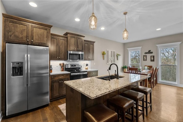 kitchen featuring tasteful backsplash, dark brown cabinets, dark wood-type flooring, stainless steel appliances, and a sink