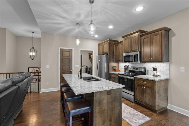 kitchen with a sink, a kitchen island with sink, stainless steel appliances, dark wood-type flooring, and backsplash