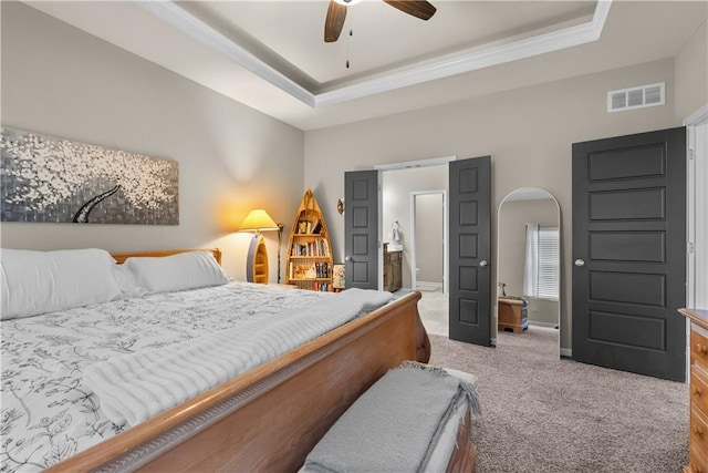carpeted bedroom with crown molding, a tray ceiling, arched walkways, visible vents, and baseboards