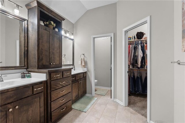 bathroom featuring vanity, a spacious closet, vaulted ceiling, toilet, and tile patterned floors