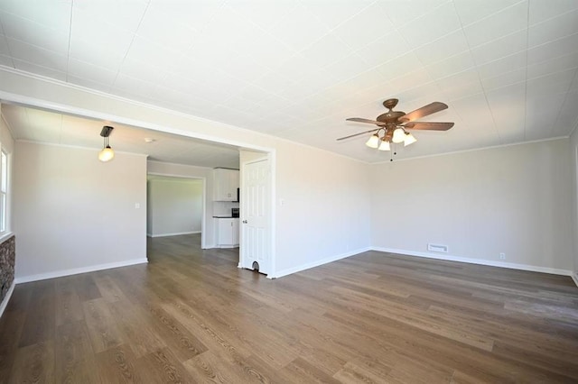 unfurnished living room with a ceiling fan, dark wood-style flooring, baseboards, and ornamental molding