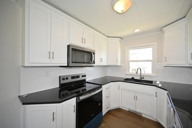 kitchen with a sink, stainless steel microwave, white cabinetry, and electric range oven