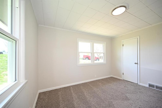 carpeted spare room featuring plenty of natural light, visible vents, and ornamental molding