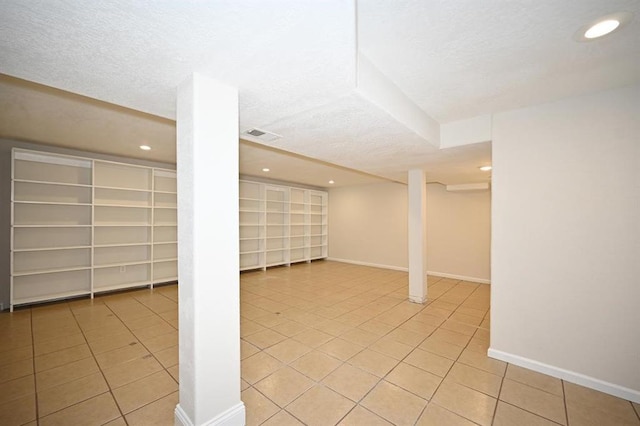 finished below grade area with a textured ceiling, light tile patterned floors, baseboards, and recessed lighting