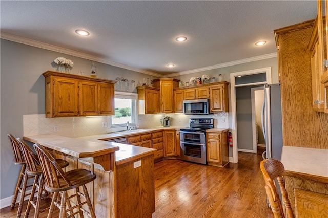 25477 Crestview Dr, Paola, KS 66071 - kitchen with appliances with stainless steel finishes, a peninsula, a sink, brown cabinets, and ornamental molding
