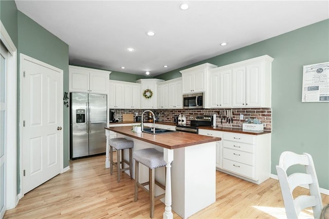 kitchen with appliances with stainless steel finishes, butcher block countertops, backsplash, white cabinets, and recessed lighting
