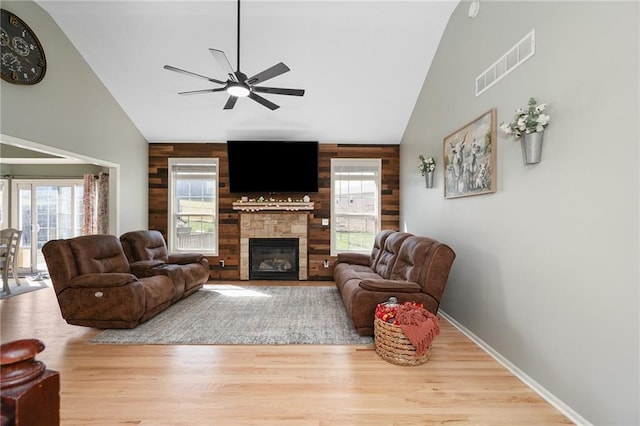 living area featuring high vaulted ceiling, wood walls, a ceiling fan, wood finished floors, and a fireplace