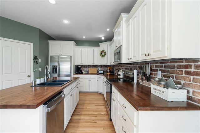 kitchen featuring butcher block counters, appliances with stainless steel finishes, a sink, a kitchen island with sink, and white cabinetry