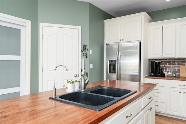 kitchen featuring stainless steel fridge with ice dispenser, a sink, wood counters, white cabinets, and tasteful backsplash