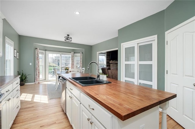 kitchen featuring butcher block countertops, a sink, light wood finished floors, white cabinetry, and stainless steel dishwasher