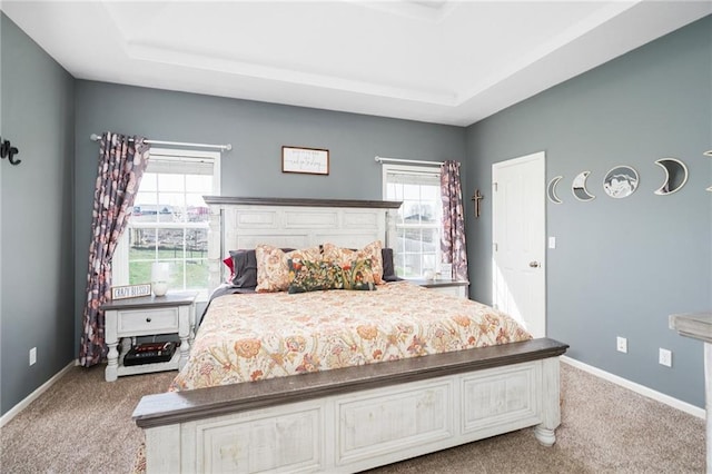 carpeted bedroom with a tray ceiling and baseboards