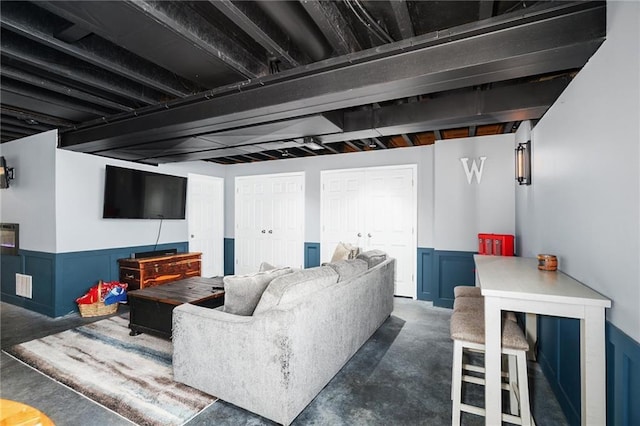 living area with concrete flooring and a wainscoted wall