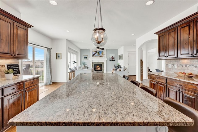 1237 Hillmann Ln, Warrensburg, MO 64093 - kitchen featuring light stone counters, recessed lighting, tasteful backsplash, a large island, and a lit fireplace