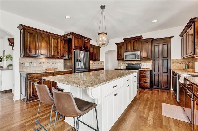 1237 Hillmann Ln, Warrensburg, MO 64093 - kitchen with stainless steel appliances, a kitchen island, arched walkways, decorative backsplash, and white cabinetry