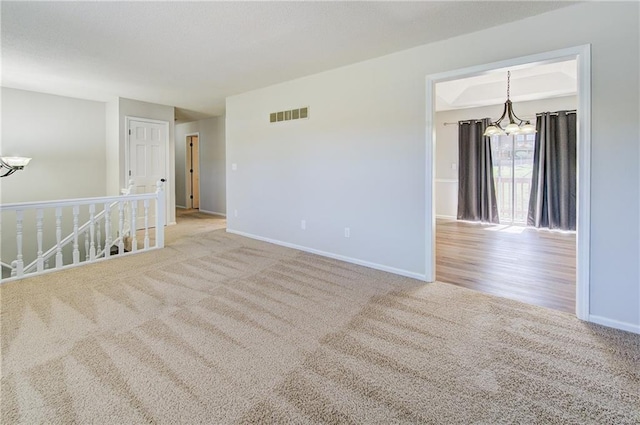 empty room with an inviting chandelier, baseboards, carpet, and visible vents